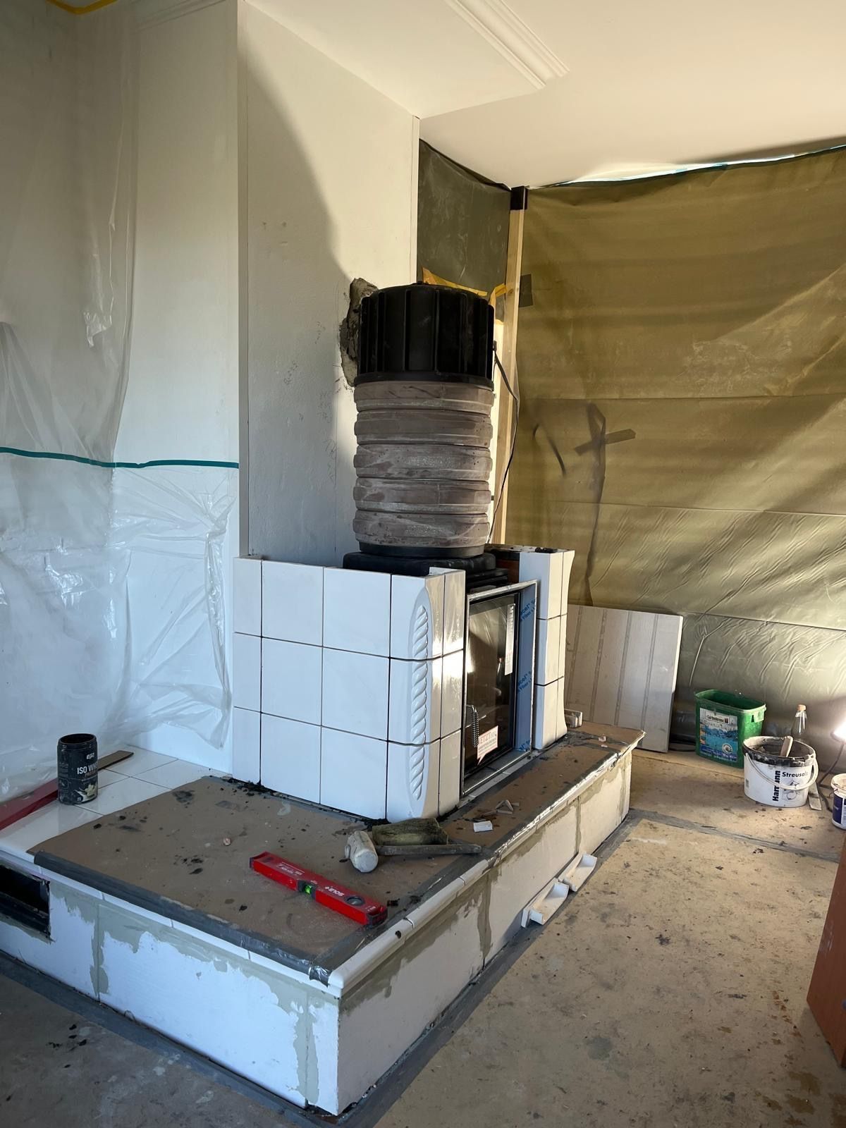 Kamin im Bau, weiße Fliesen verlegt, graue Kaminplatte, schwarzer Schornstein. Arbeitsbereich.