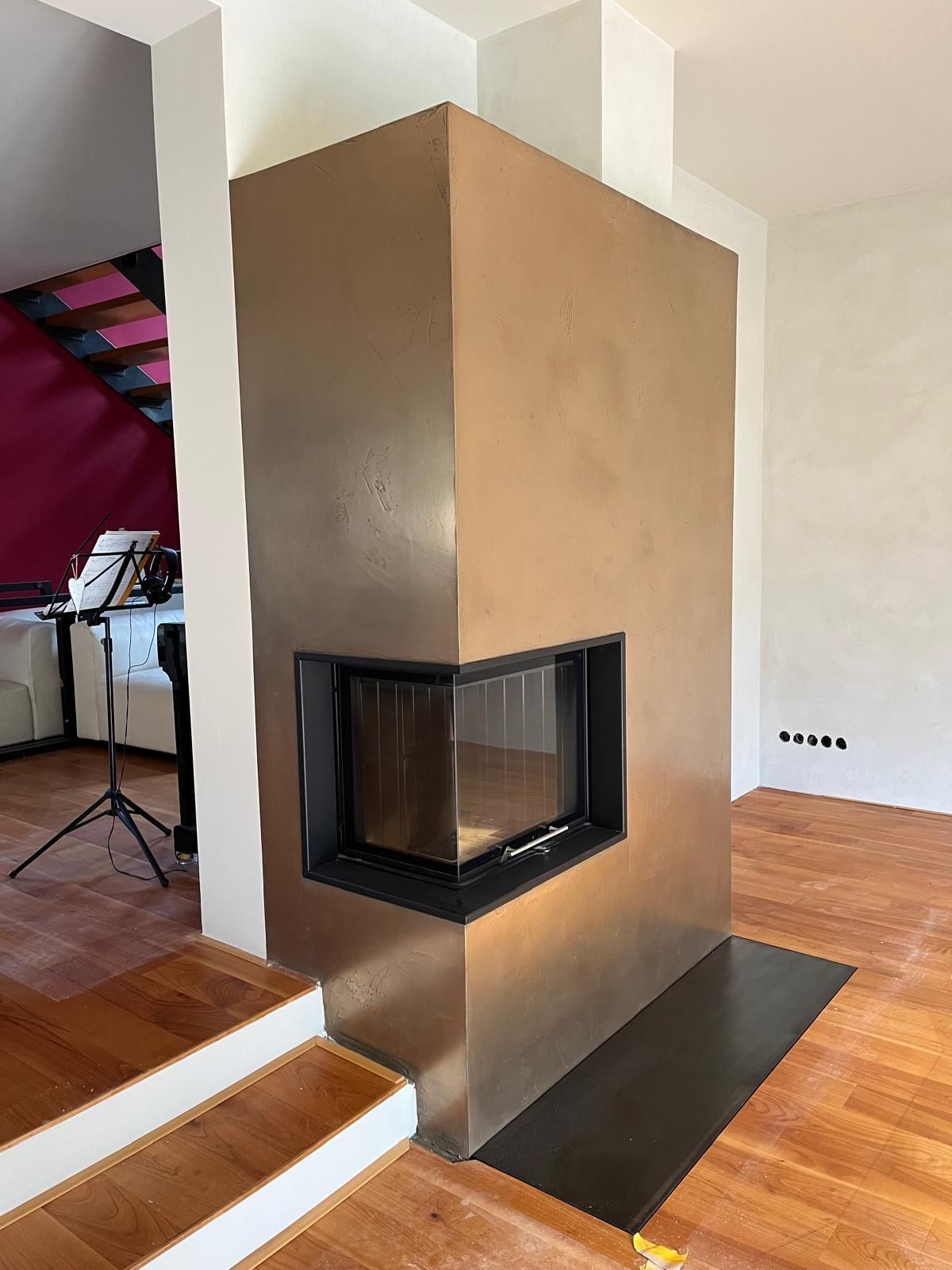 Eckkamin mit bronzefarbener Oberfläche, schwarzem Zierrahmen und Sichtfenster aus Glas.