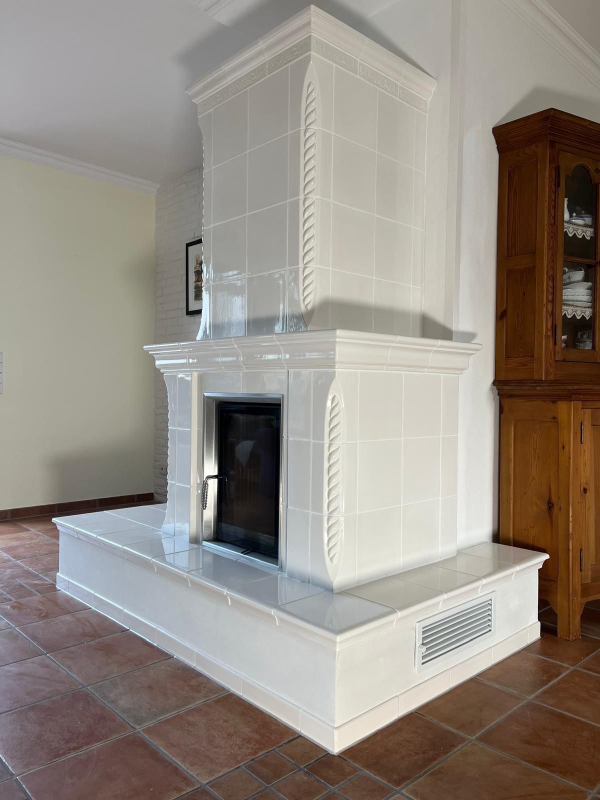 Weiß gefliester Kamin mit dekorativen Verzierungen in einem Raum mit Terrakottafliesenboden.