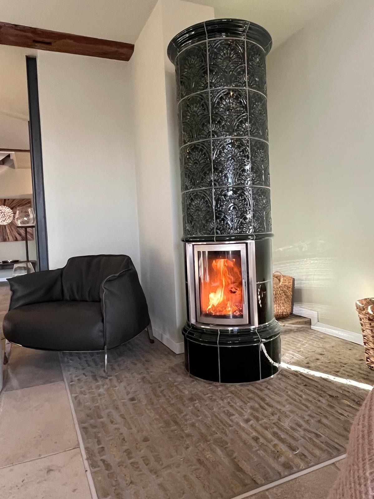 Hoher, schwarzer Kamin mit Flammen, daneben ein schwarzer Ledersessel.