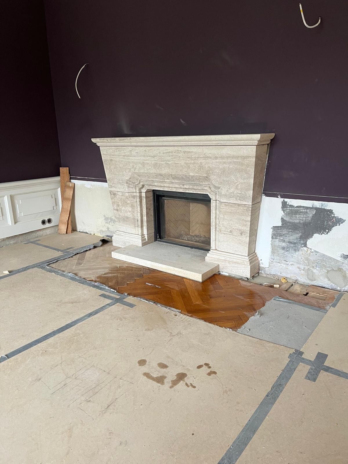 Kamin mit heller Steineinfassung vor einer dunkelvioletten Wand. Bauschutt auf dem Boden.