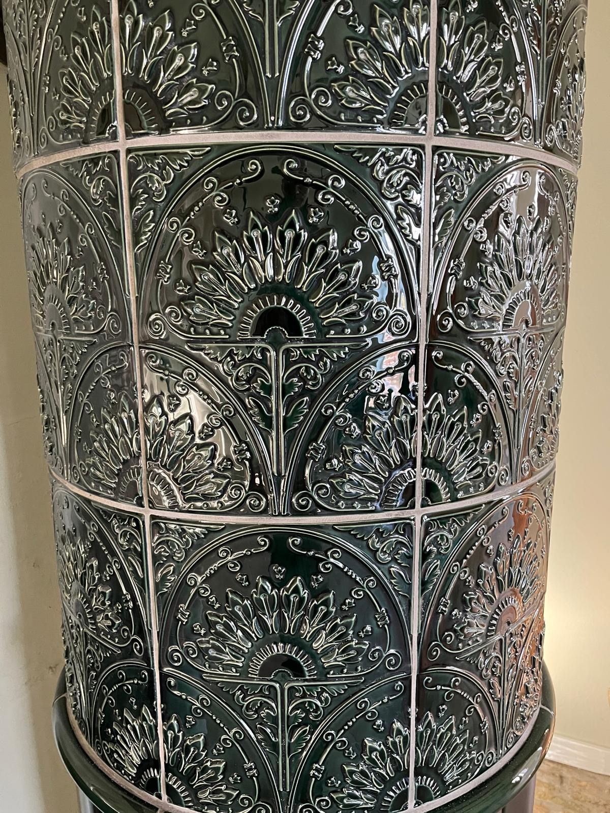 Dunkelgrüner, reich verzierter Kachelofen mit weißen Fugen.