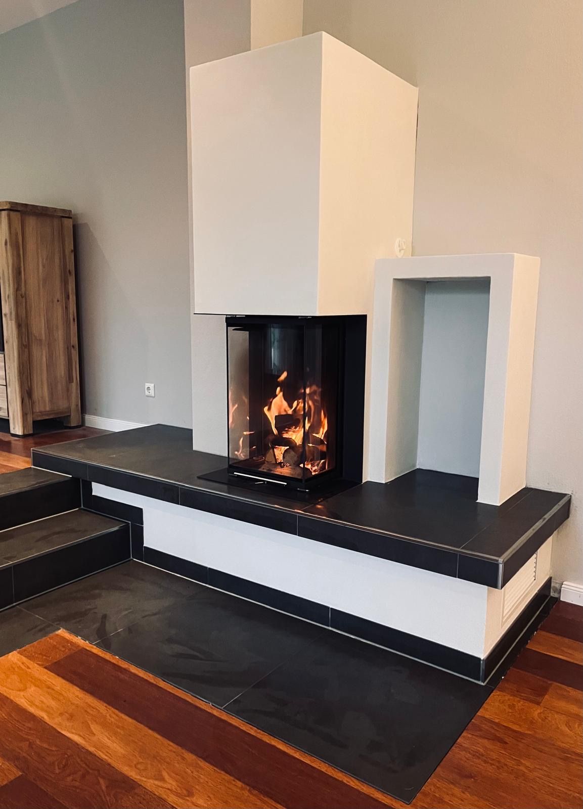 Moderner Kamin mit weißer Umrandung und dunkler Feuerstelle, in dem ein Feuer brennt.