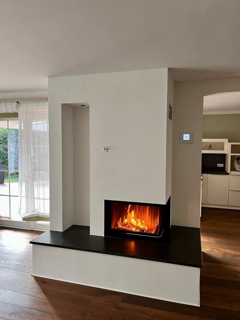 Moderner Kamin mit Feuerstelle, in weiße Wand eingelassen, schwarze Feuerstelle, zu den Räumen hin offen.