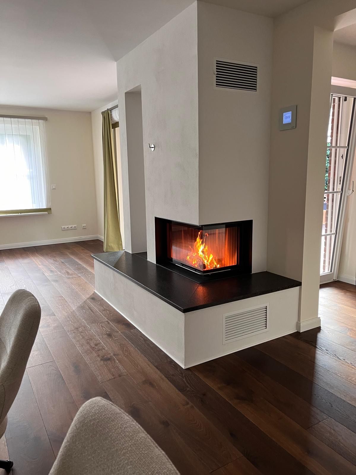 Moderner Kamin mit prasselndem Feuer, eingebaut in eine weiß-dunkle Steinkonstruktion, in einem Raum mit Holzboden.