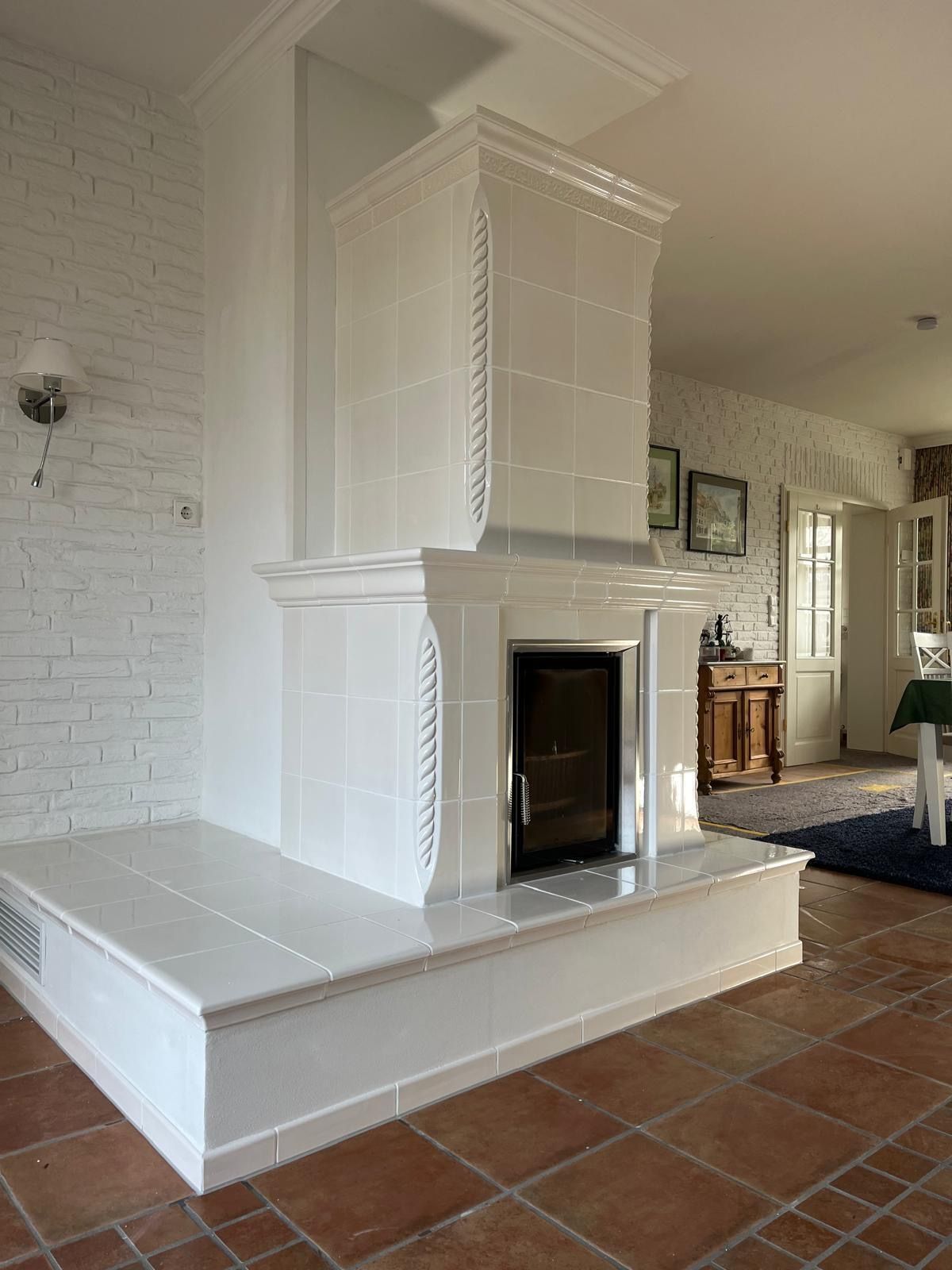 Ein weiß gefliester Kamin in einem Raum mit Terrakottafliesenboden und einer weißen Ziegelwand.