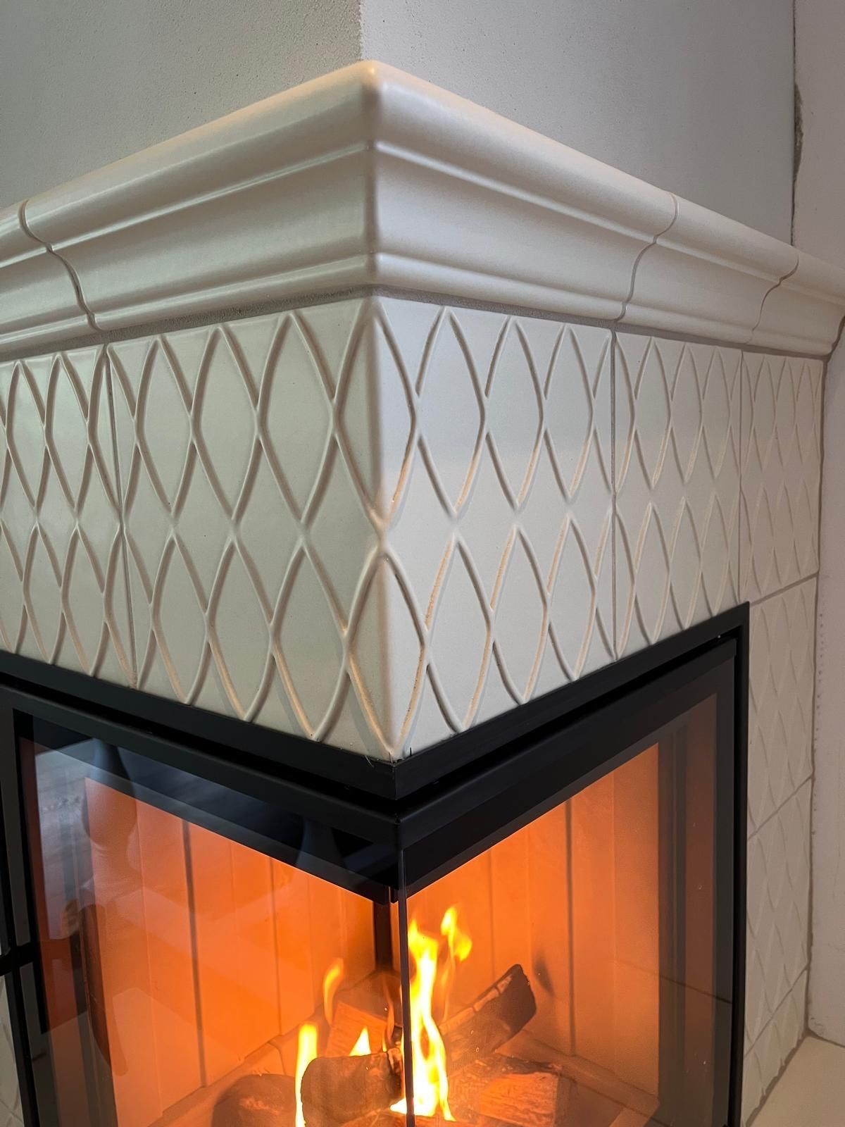 Kamin mit weißen, gemusterten Fliesen und einem brennenden Feuer.