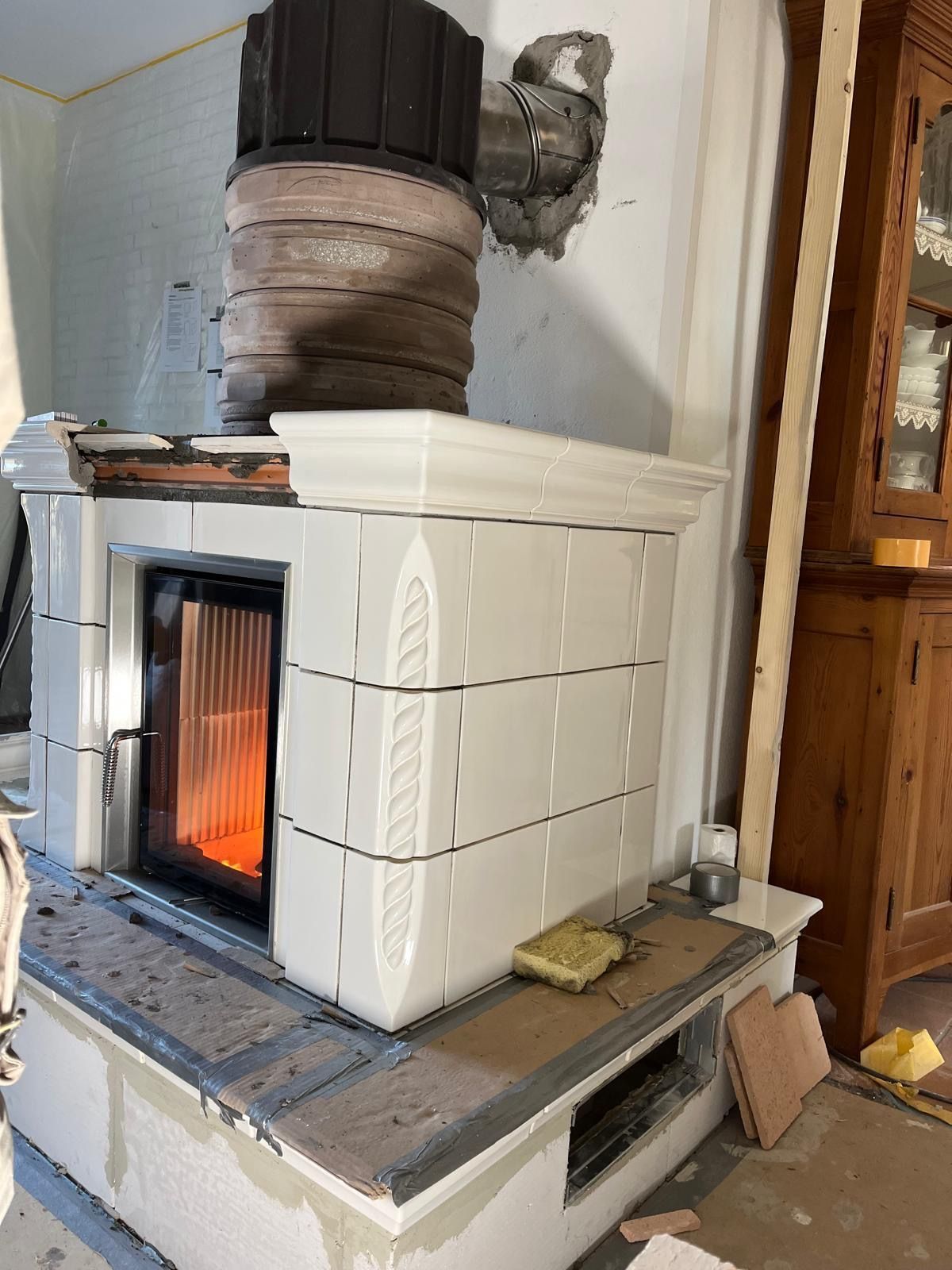 Weiß gefliester Kamin mit brennendem Feuer, Metallelementen und Schornstein, im Bau befindlicher Innenbereich.