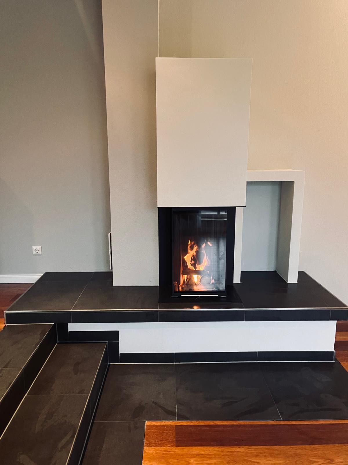 Moderner Kamin mit schwarzen Fliesenstufen und -herdplatte, Flammen im Inneren sichtbar. Weiß und Grau.