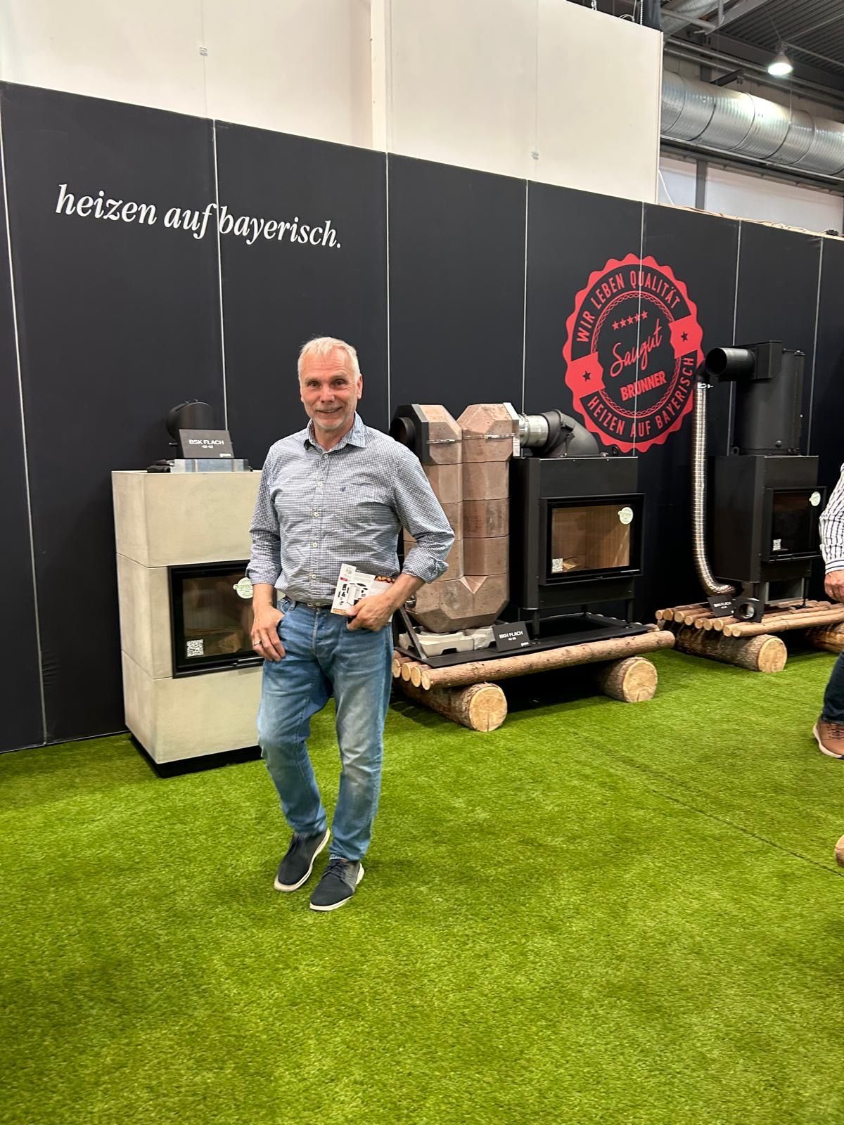 Ein Mann steht vor Öfen an einem Messestand mit schwarzer Wand und künstlichem grünen Gras.