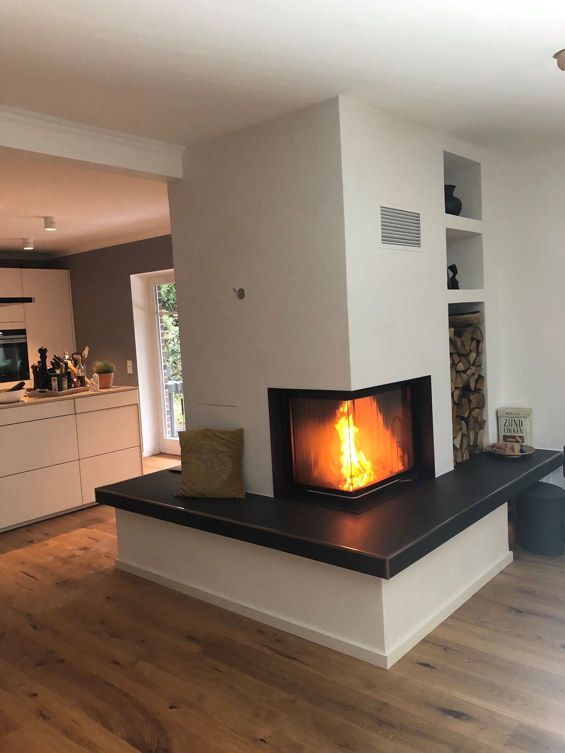 ein Wohnzimmer mit Kamin und eine Küche im Hintergrund