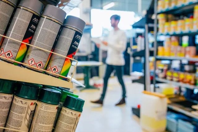 Gros plan sur des bombes de peinture sur une étagère dans un magasin, avec une personne floue qui marche en arrière-plan.