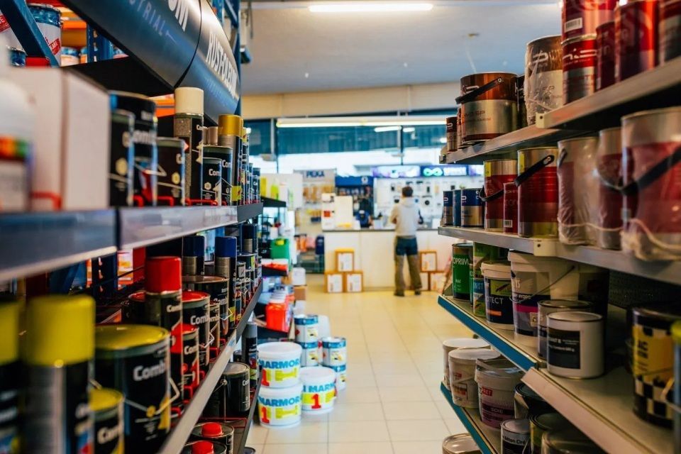 Vue d'une allée d'une quincaillerie remplie de pots de peinture et de fournitures, avec une personne debout au comptoir.