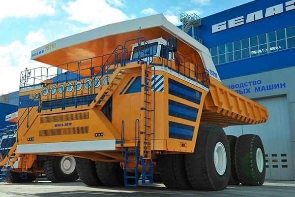 Un gran camión volquete amarillo está estacionado frente a un edificio que dice gena