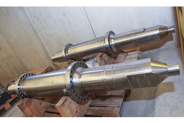 Dos grandes ejes de metal se encuentran encima de paletas de madera.