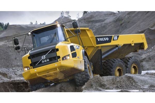 Un camión volquete Volvo amarillo circula por un campo de tierra.