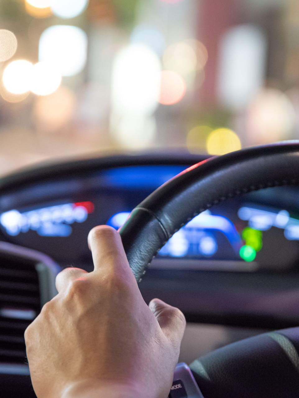 Main sur le volant, conduite de nuit. Tableau de bord et lampadaires en arrière-plan.
