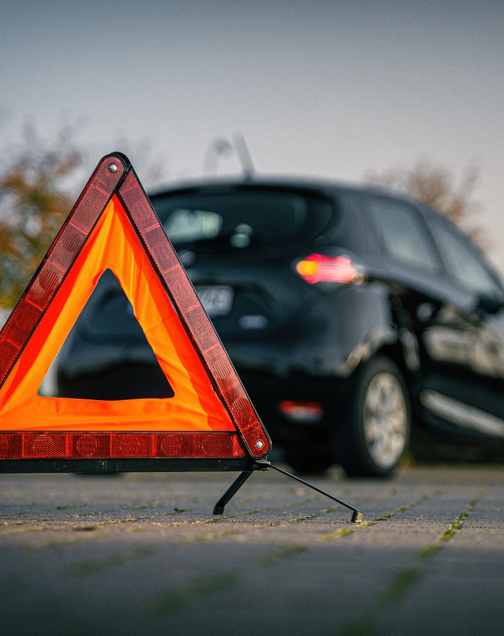 Triangle de signalisation devant une voiture noire en panne sur une route goudronnée.