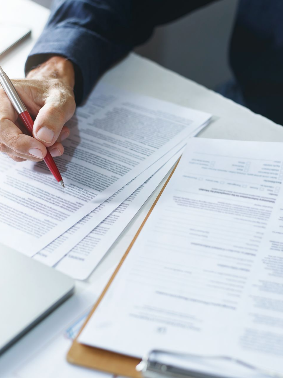 Une personne signe des documents à un bureau, avec un ordinateur portable et des papiers.