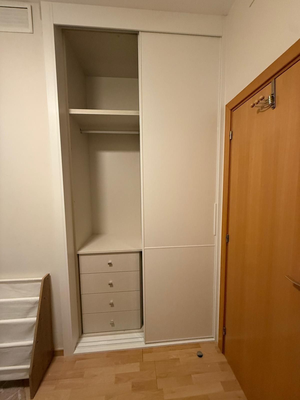 Pequeño armario con estantes y cajones junto a una puerta de madera en una habitación de color beige.