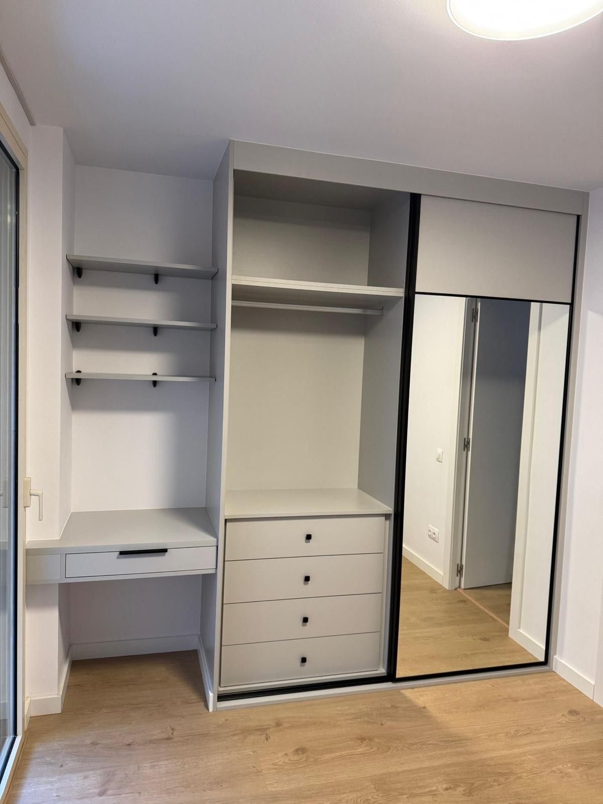 Vestidor con estantes blancos, cajones y puertas corredizas con espejo sobre un piso de madera.