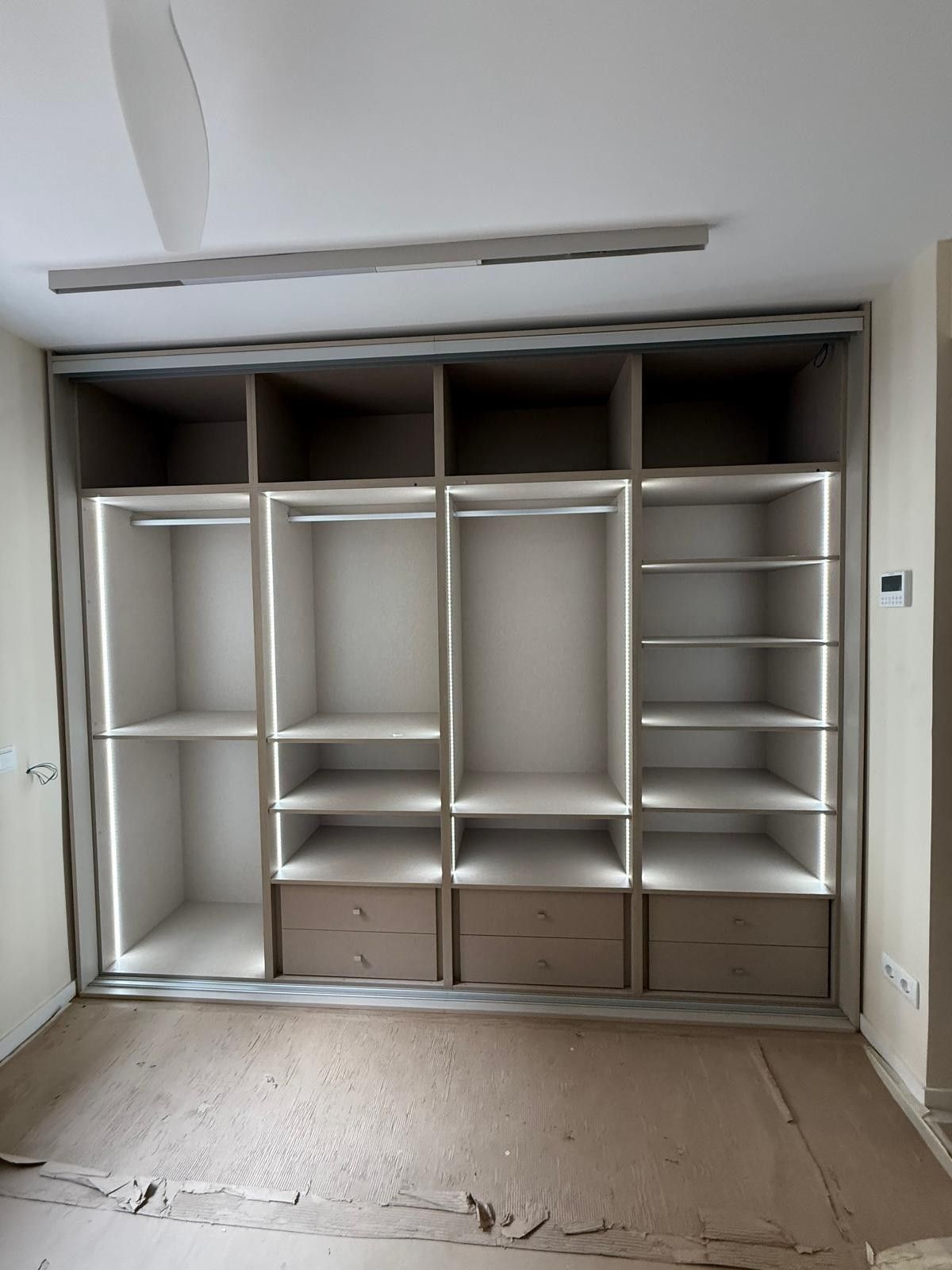 Armario empotrado vacío con estantes, barras para colgar ropa y cajones en una habitación diáfana en proceso de reforma.