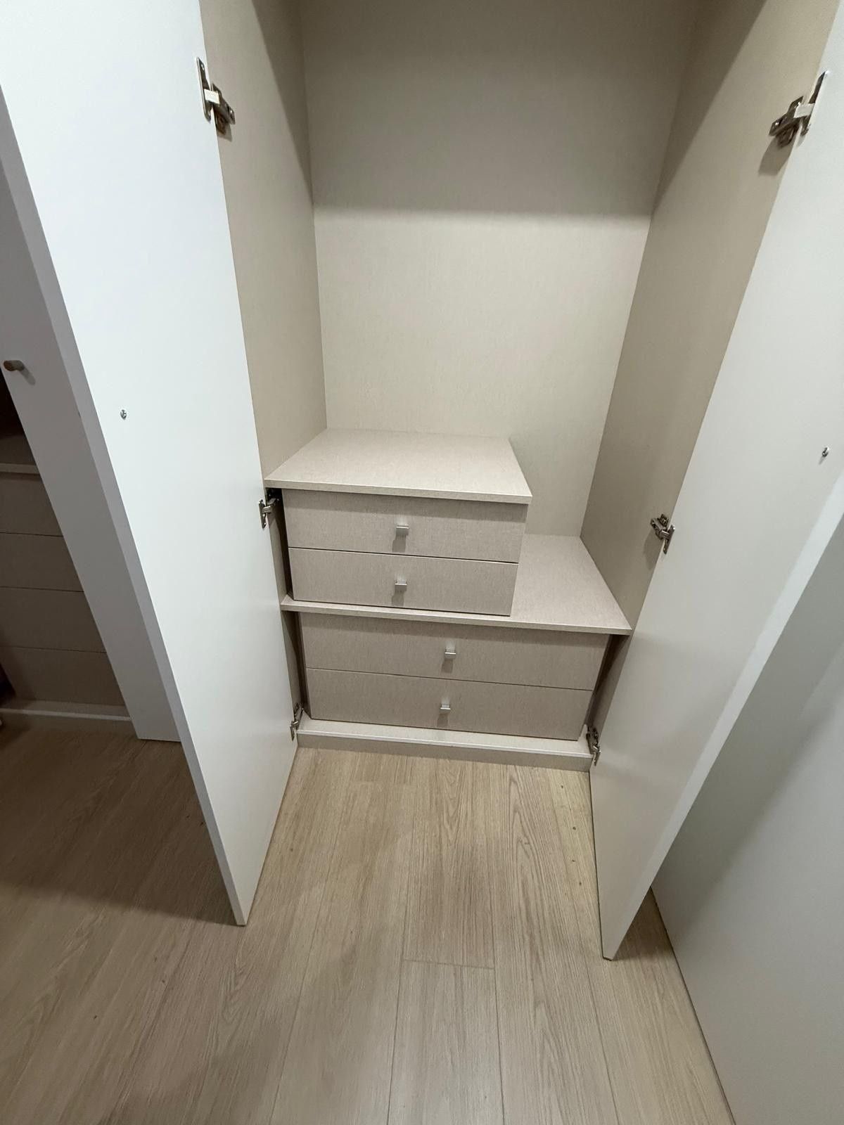 Armario abierto con estantes y cajones blancos sobre un suelo de madera clara.