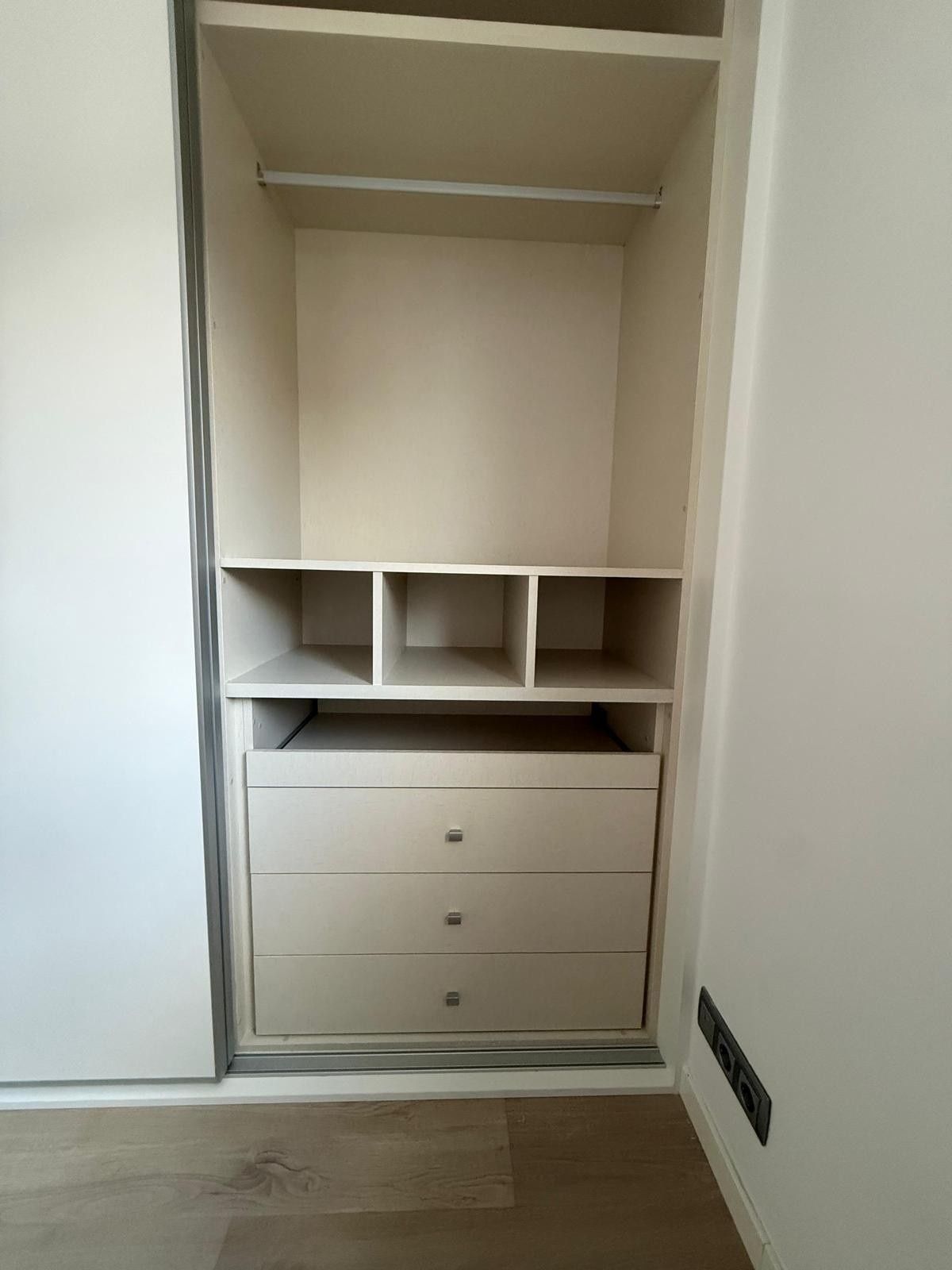 Armario empotrado con estantes, compartimentos y tres cajones en una habitación blanca.