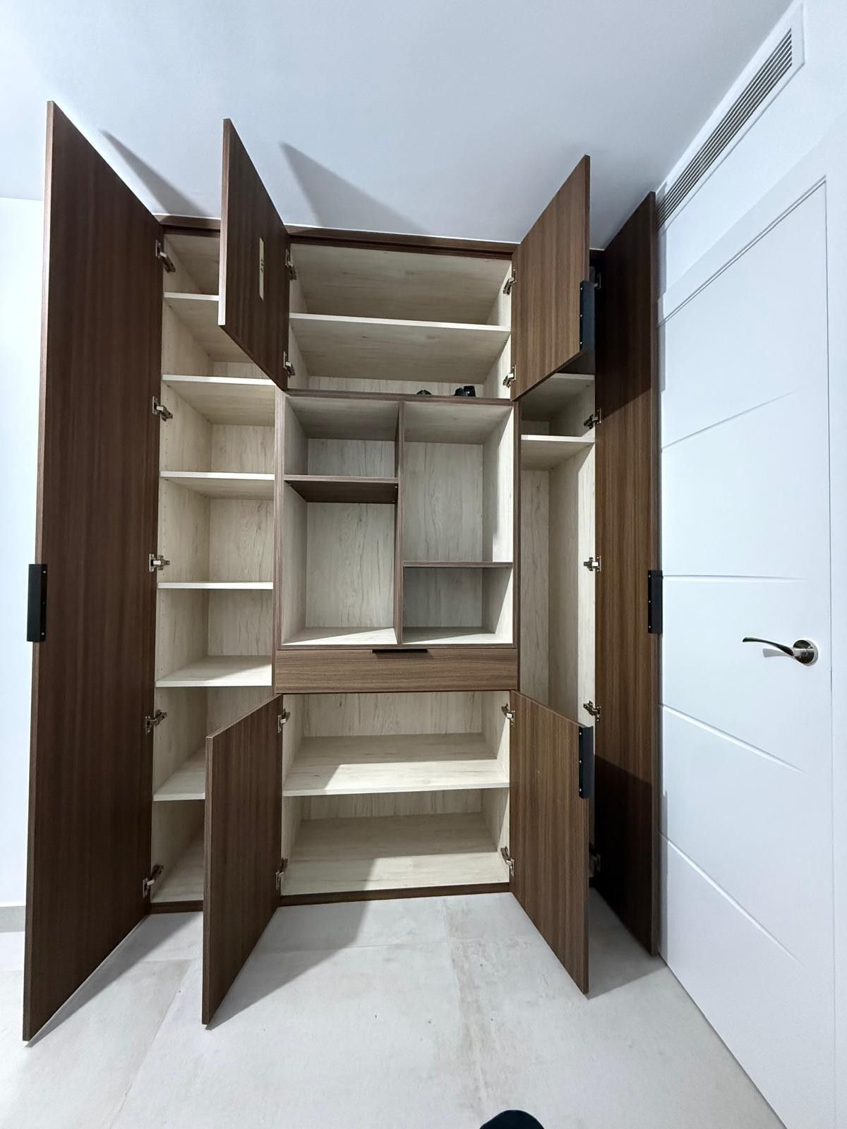 Armario abierto de madera con estantes y espacio para colgar ropa en una habitación blanca.