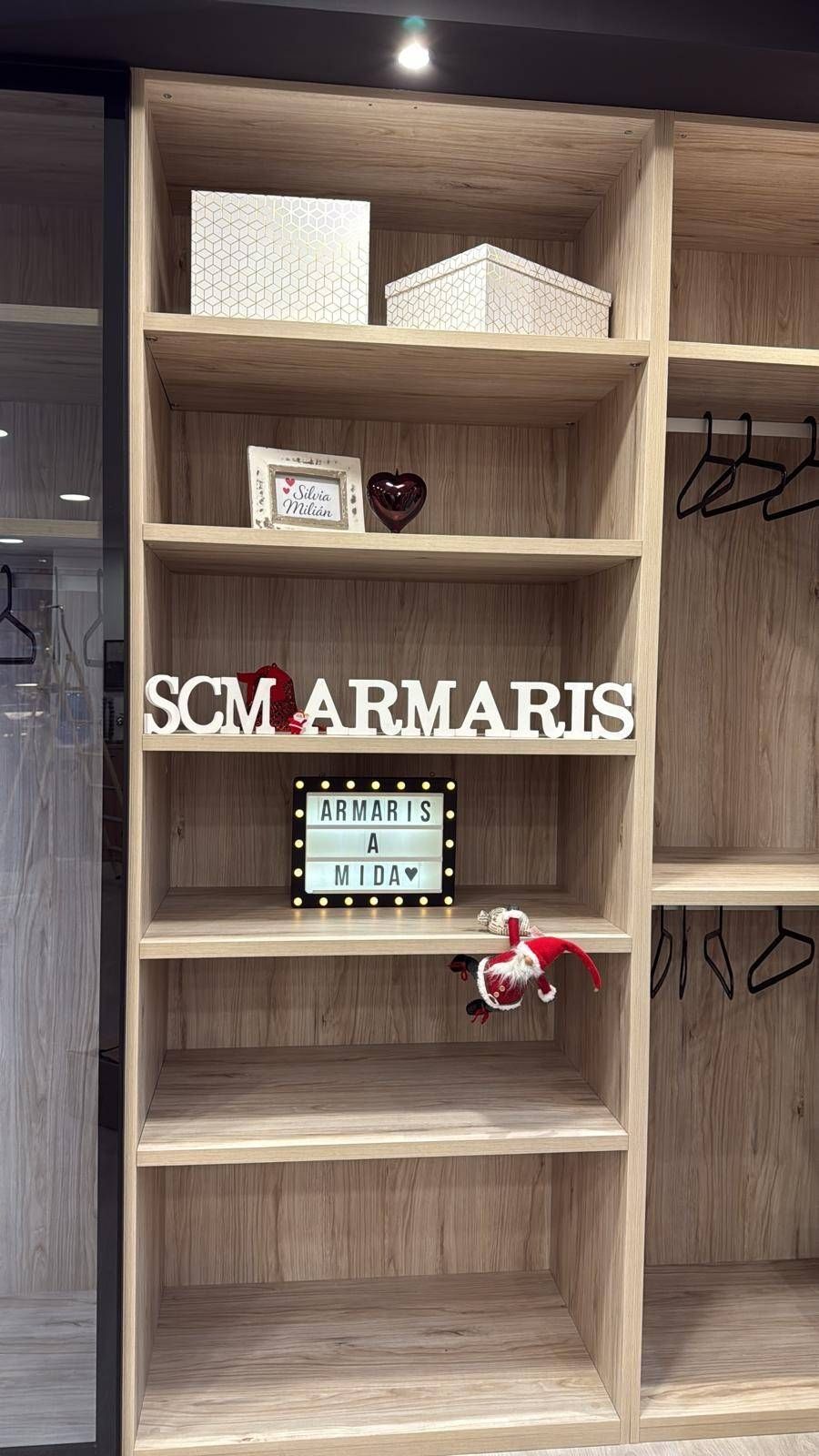 Estanterías de madera con decoración y un letrero que dice “SCM ARMARIS” en una sala de exposición.