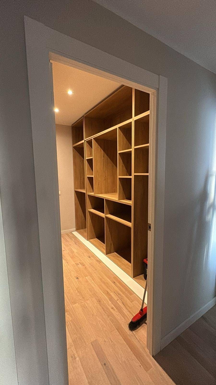 Entrada abierta a un vestidor con estantes de madera sin acabado y luces cálidas en el techo.