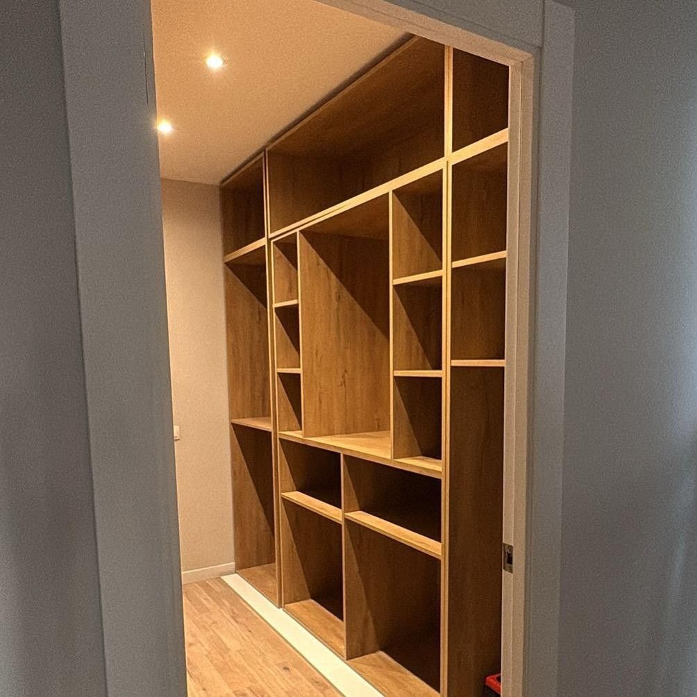 Estanterías de madera empotradas en un armario estrecho o vestidor, vistas a través de una puerta.