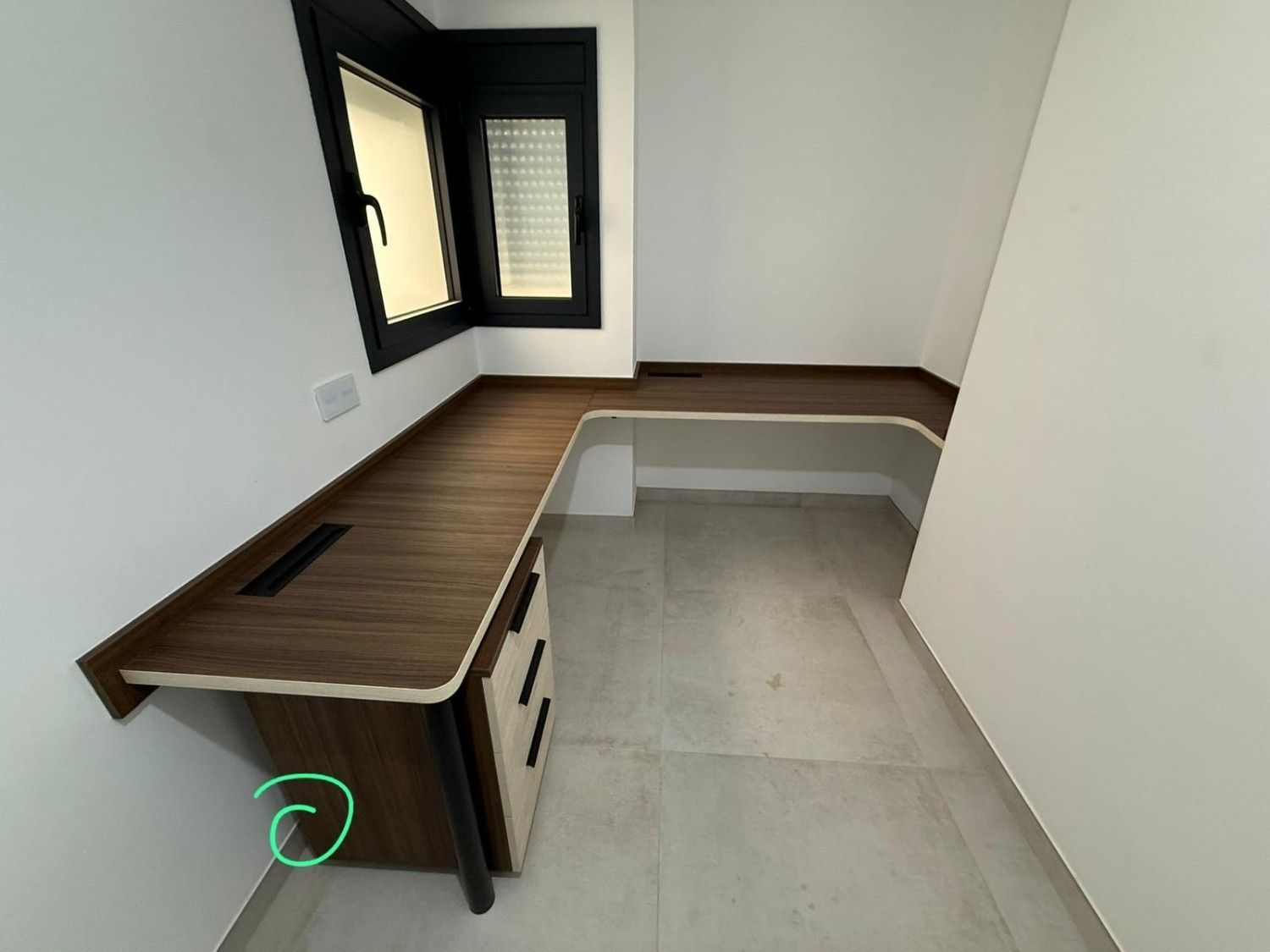 Habitación moderna vacía con escritorio de madera, suelo beige, paredes blancas y ventana con marco negro.