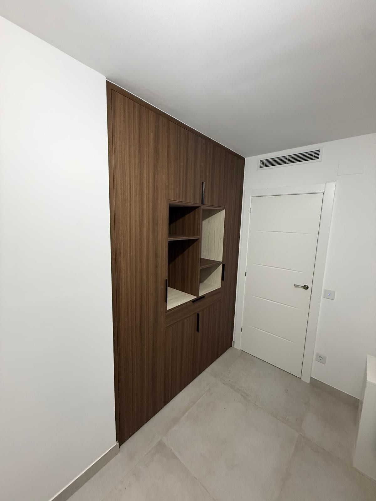 Entrada moderna con pared decorativa de madera, pequeño nicho con estante, puerta blanca y suelo de baldosas claras.