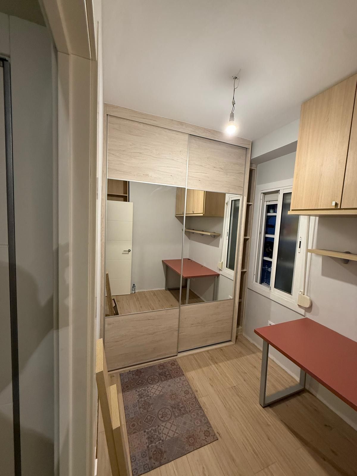 Cocina pequeña y estrecha con armarios de madera, encimeras rojas, una ventana y una puerta de armario con espejo