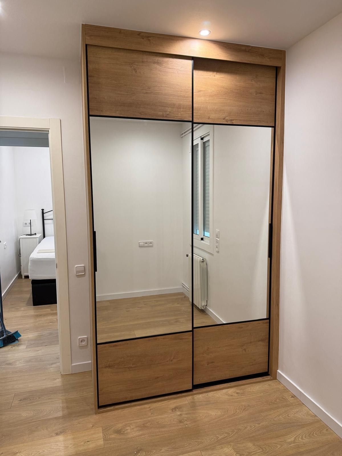 Armario de madera con espejos en una habitación minimalista con paredes blancas y suelo de madera.