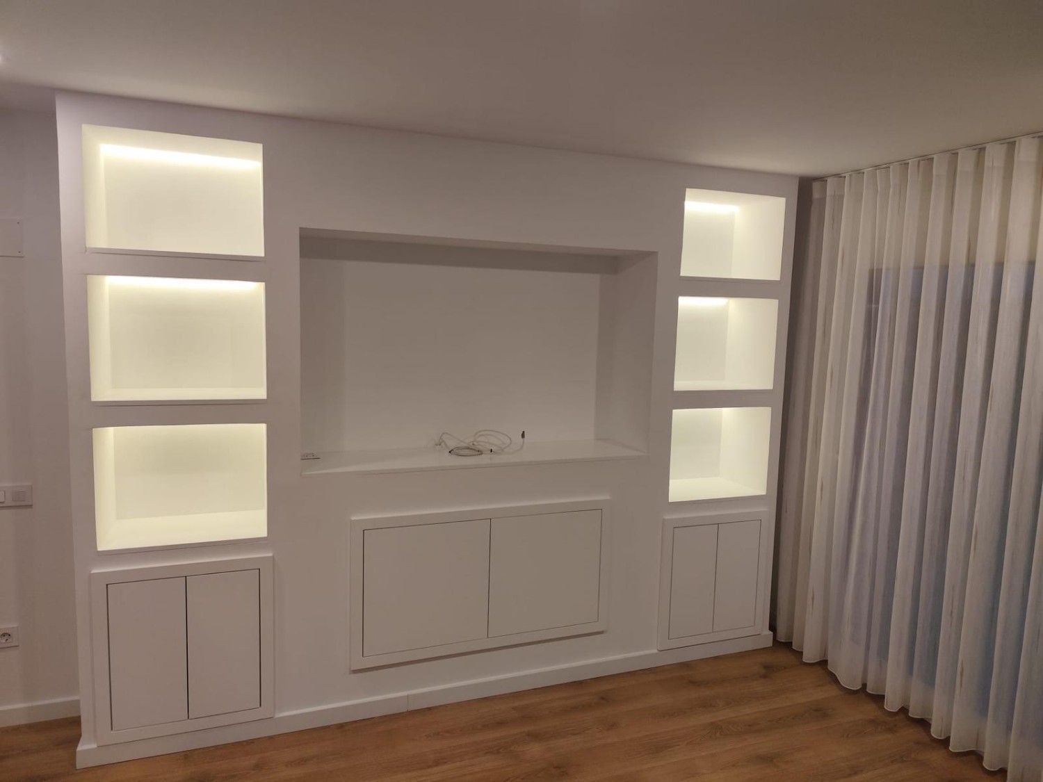 Estanterías empotradas en la pared con nichos retroiluminados y armarios en una habitación moderna