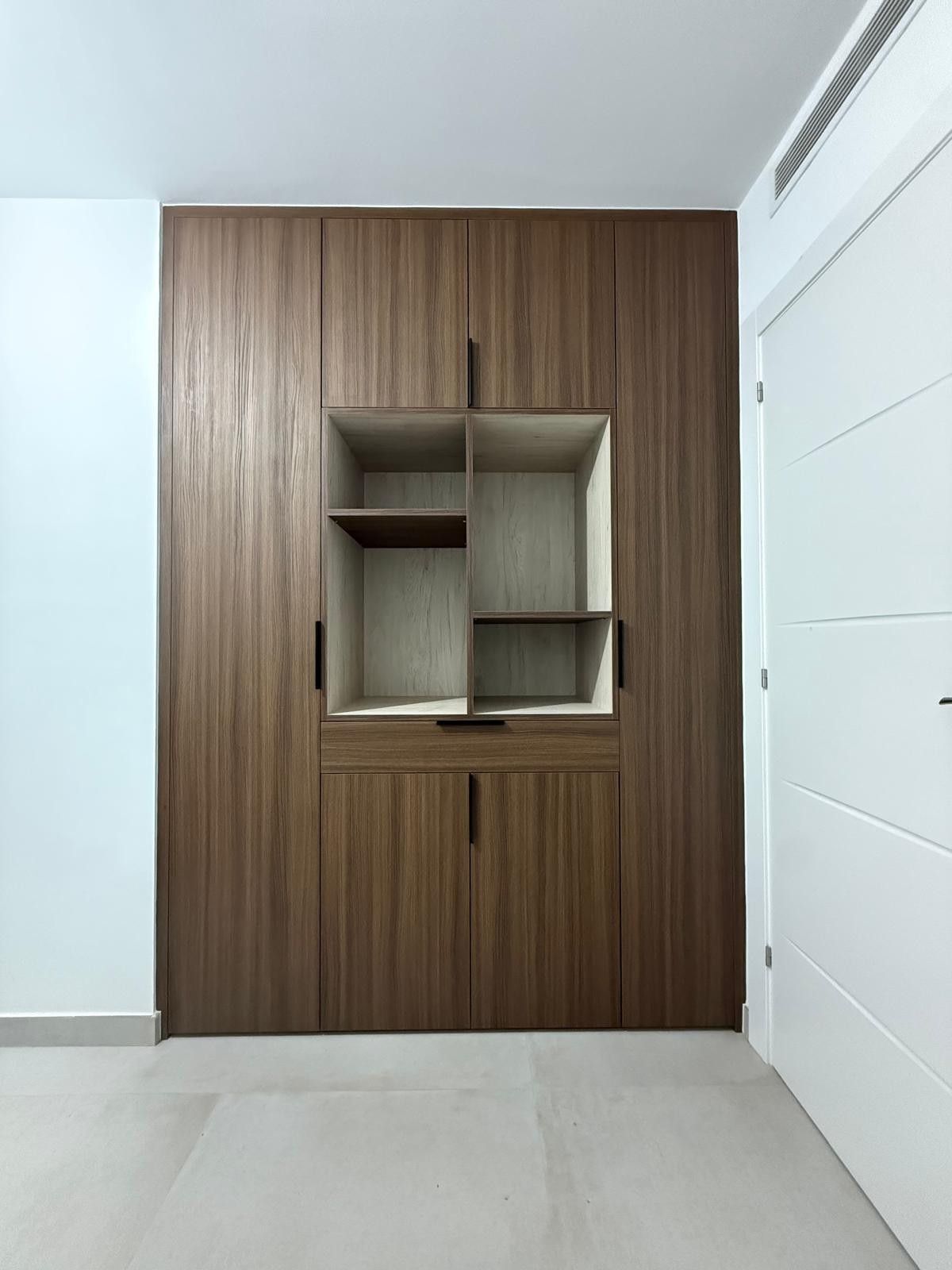 Habitación moderna con una pared revestida de madera y nichos cuadrados con estanterías empotradas junto a una puerta blanca.