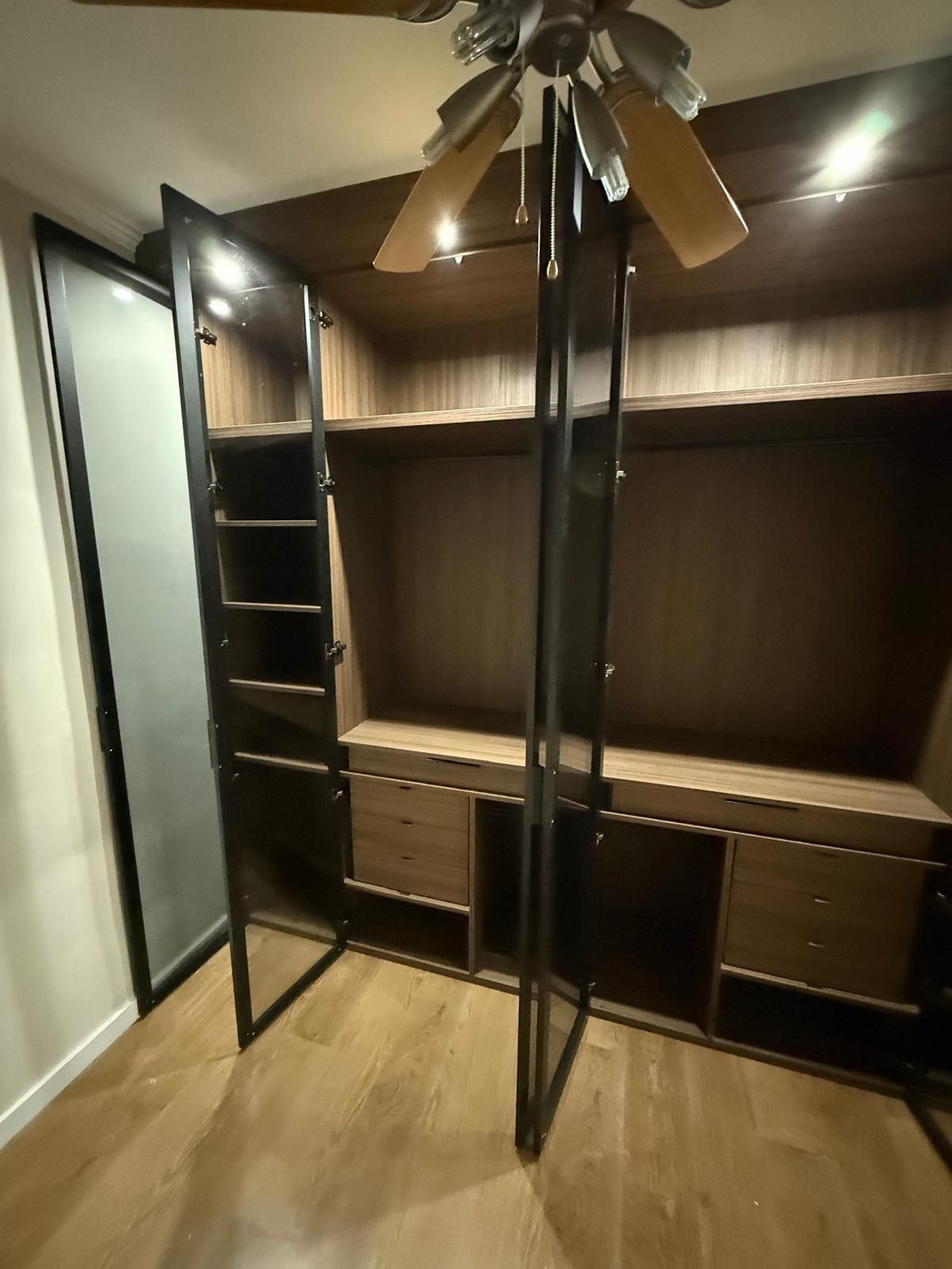 Vestidor con puertas abiertas, estantes de madera oscura y ventilador de techo.