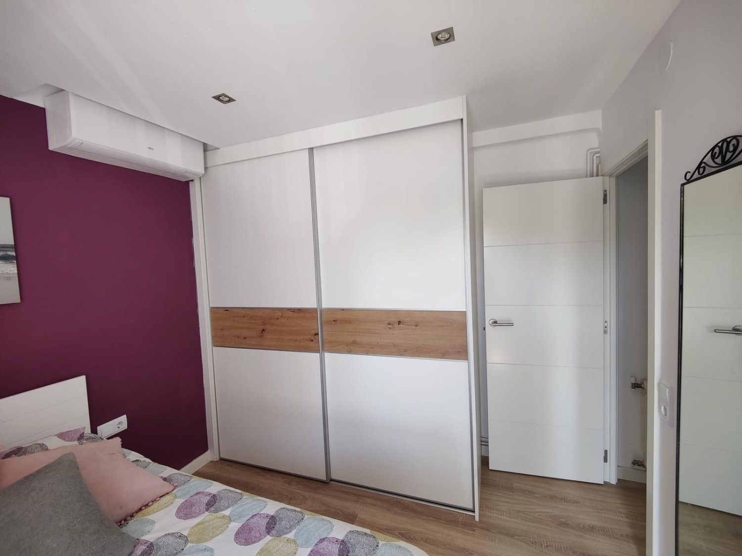 Dormitorio con armario corredero blanco, pared decorativa de color morado y una cama en la esquina.