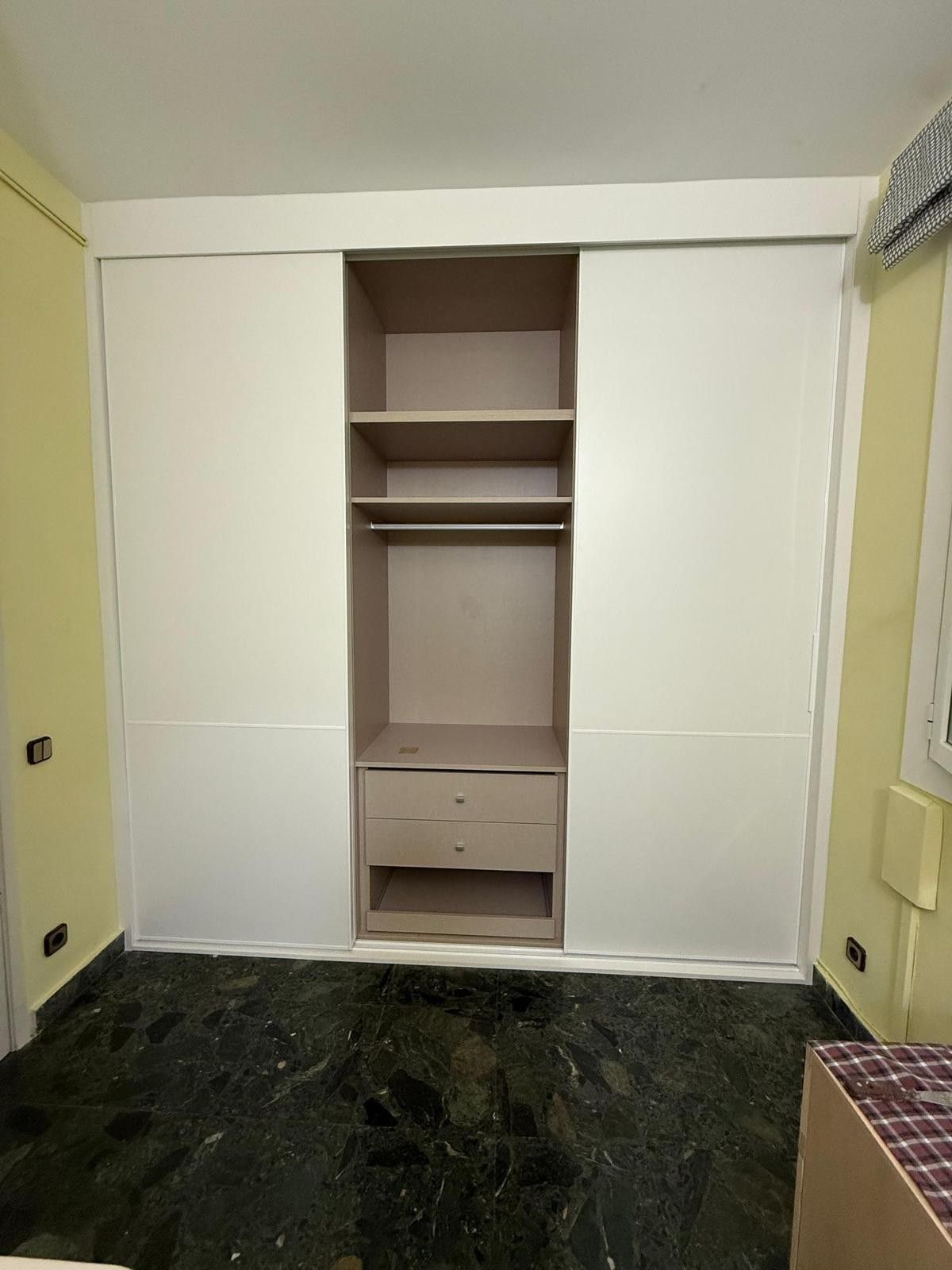 Nicho vacío de armario empotrado en una habitación con puertas blancas y suelo de mármol verde oscuro.