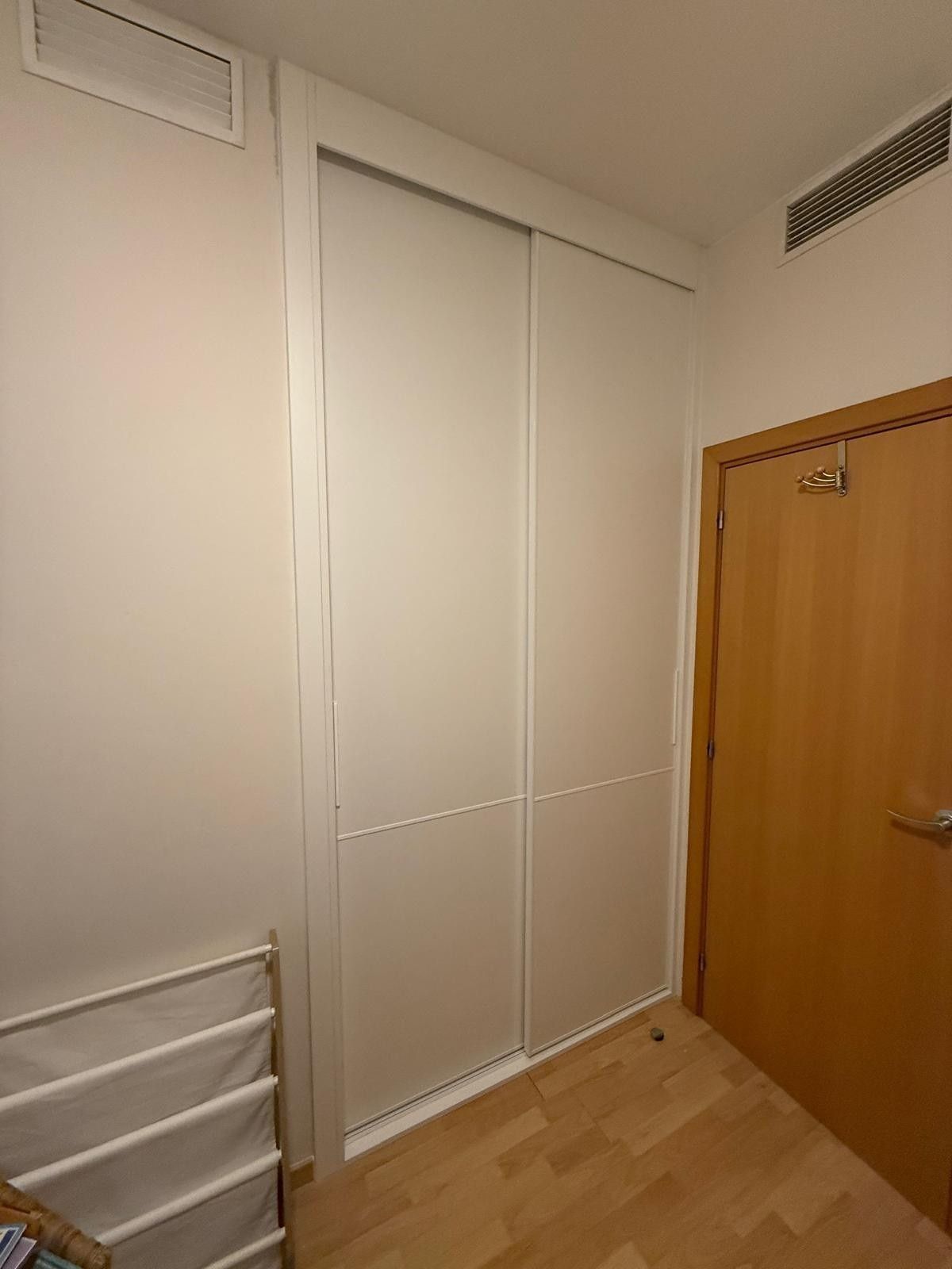Puertas blancas de armario en una habitación pequeña junto a una puerta de madera y paneles de pared ventilados.