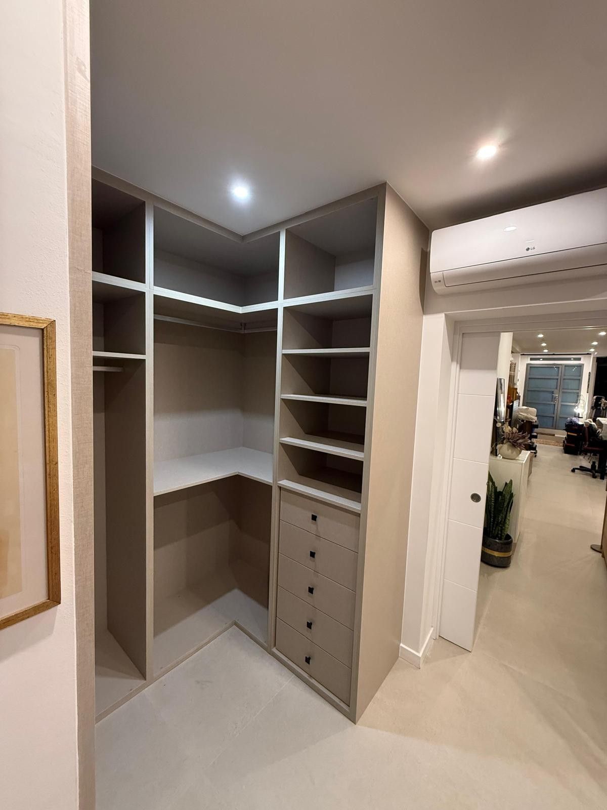 Vestidor empotrado con estantes, cajones y barras para colgar ropa de color gris en un pasillo luminoso.