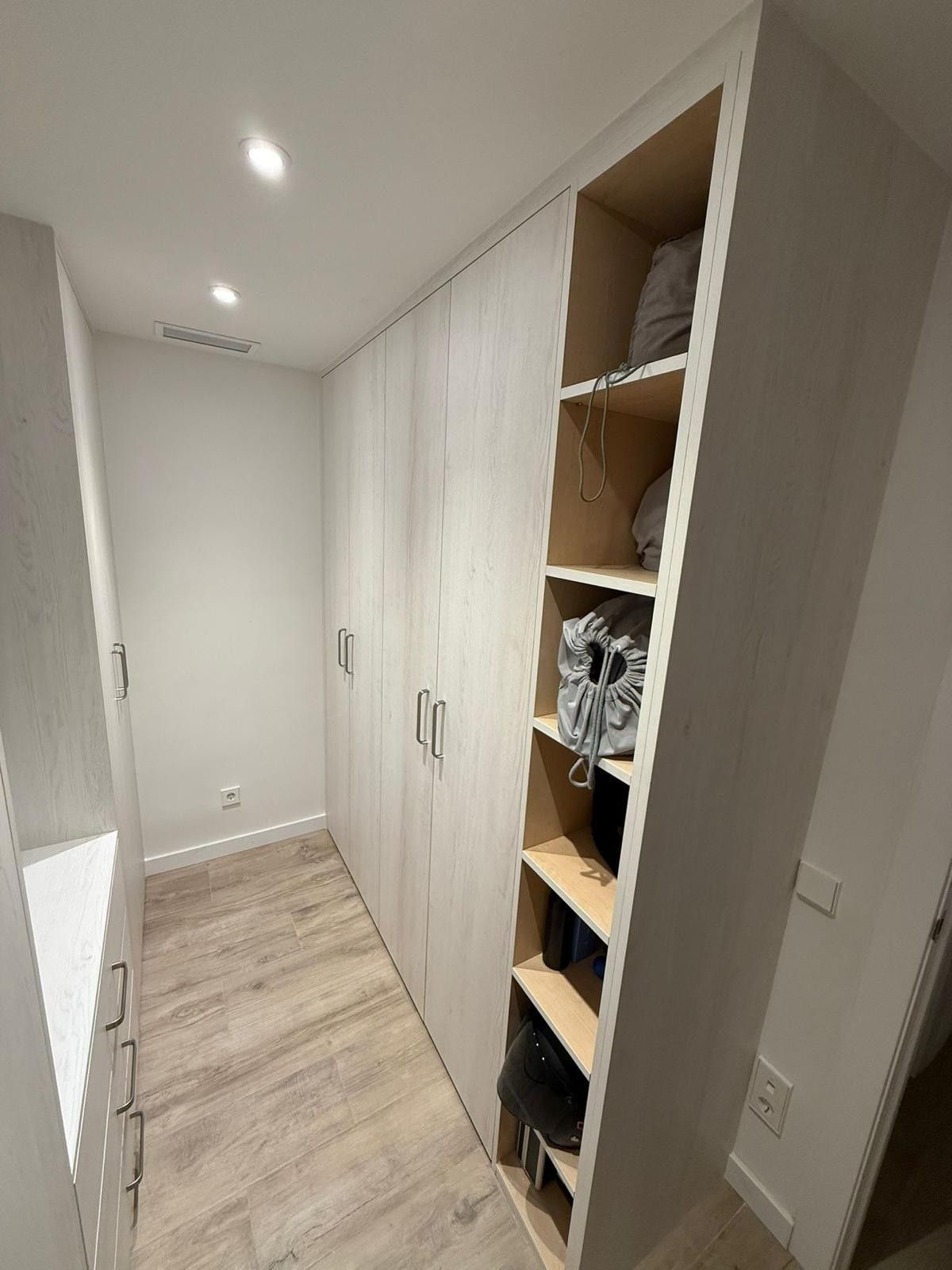 Pasillo estrecho de color blanco con suelo de madera clara y un estante abierto empotrado en un armario a la derecha.