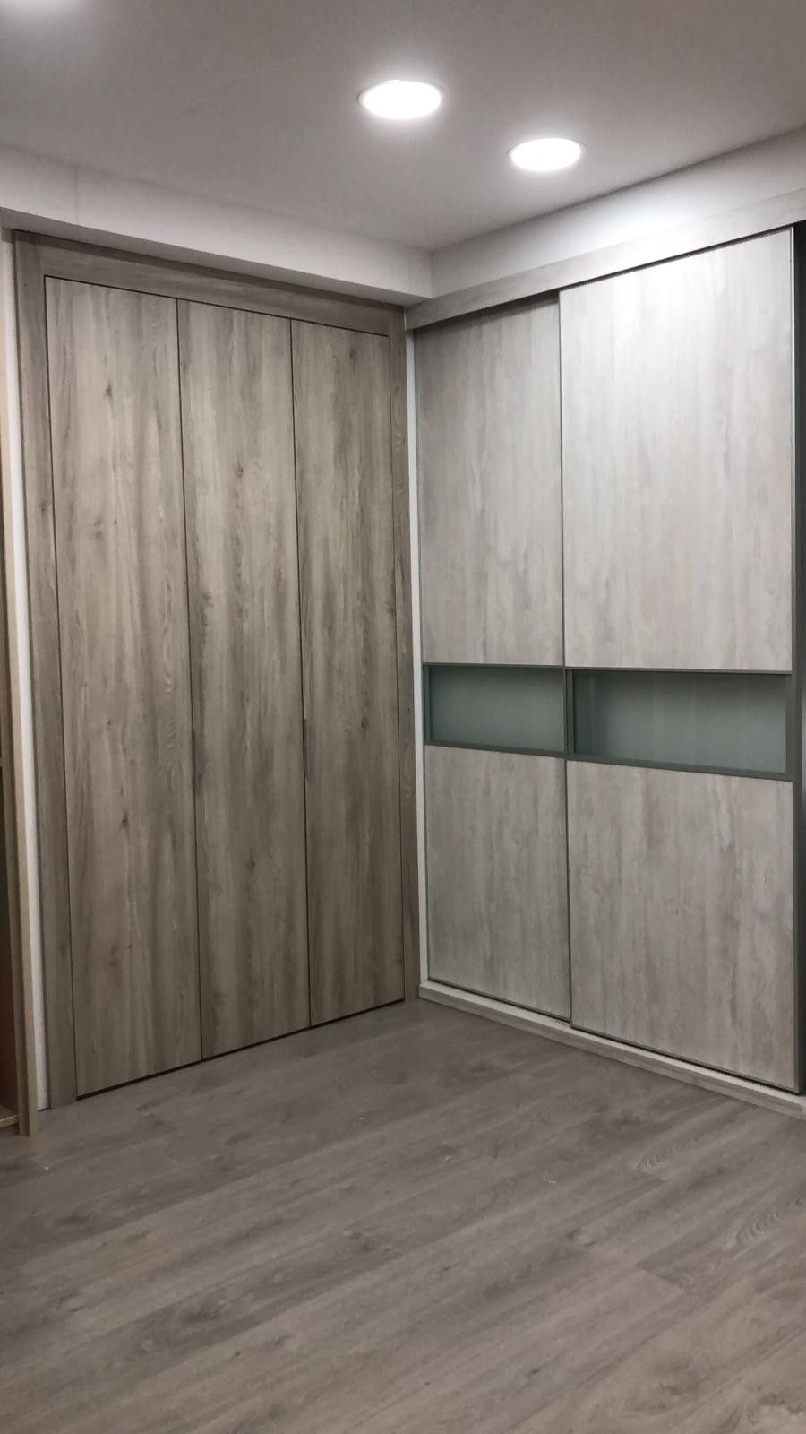 Habitación vacía con suelo de madera gris y armarios empotrados de madera clara contra la pared.