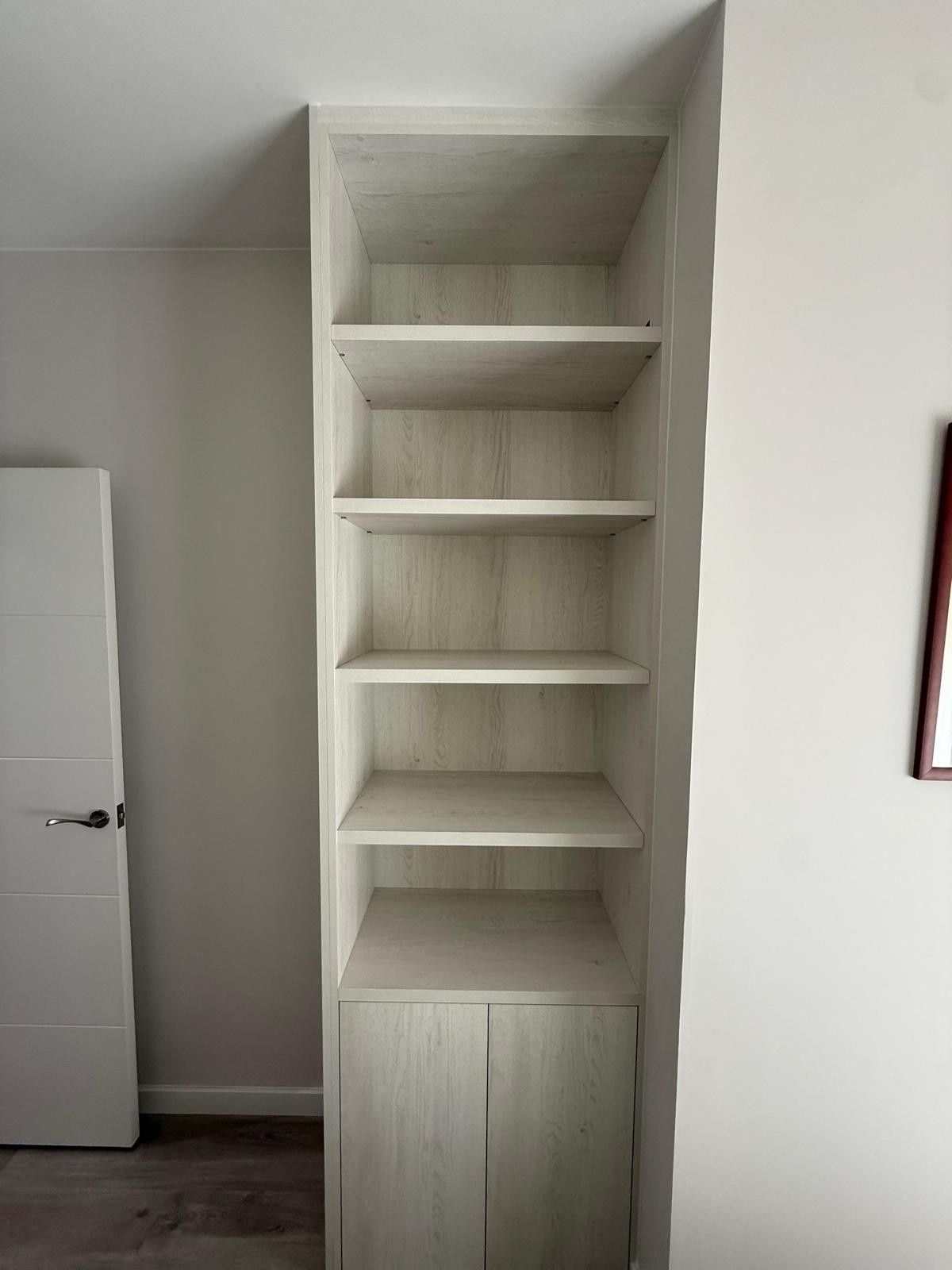 Estantería alta empotrada de color blanco con puertas de armario en una habitación, junto a una puerta abierta.