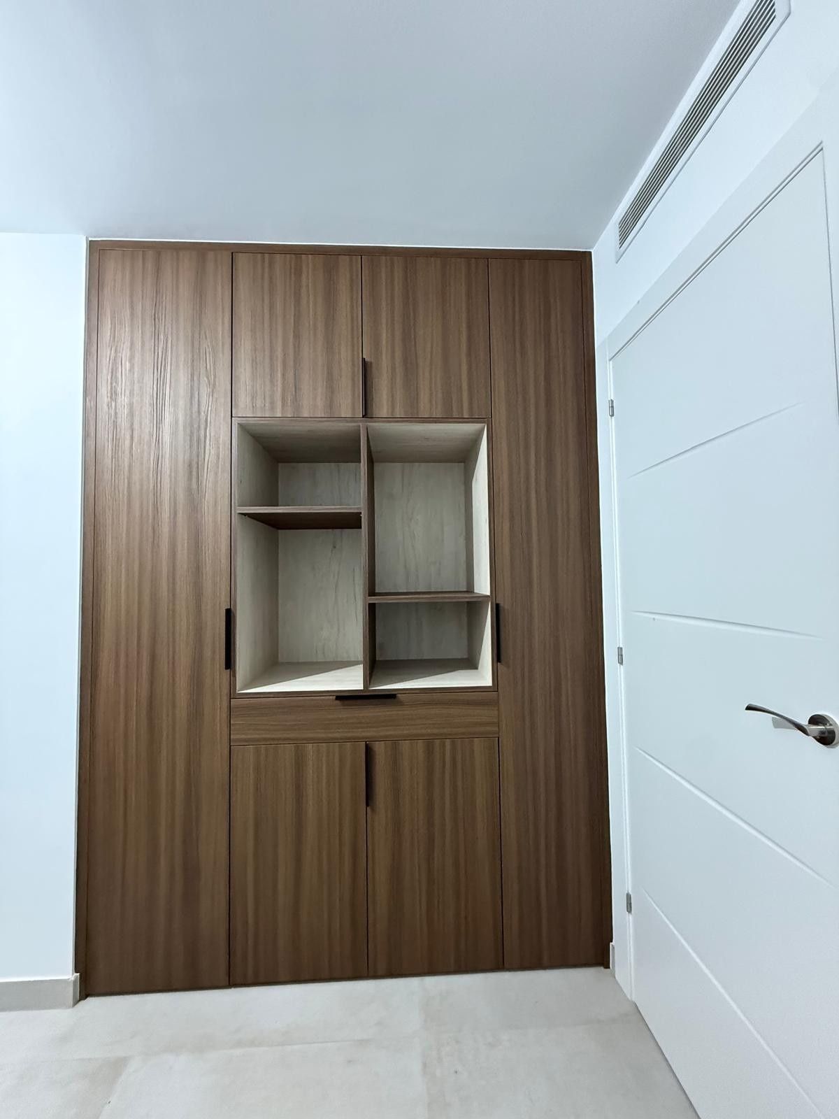 Pared revestida de madera con nicho de estanterías integradas en una habitación blanca minimalista.