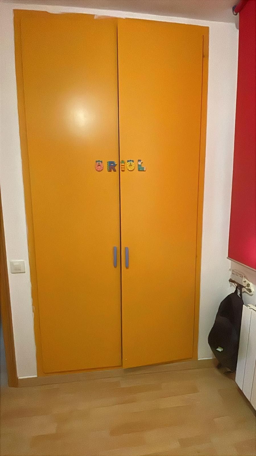Armario naranja de doble puerta con tiradores plateados en un dormitorio pequeño.
