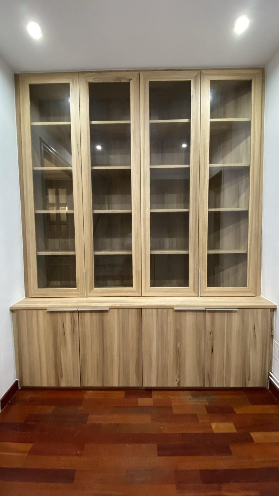 Armario empotrado de madera con estantes superiores de cristal en una habitación con suelo de madera