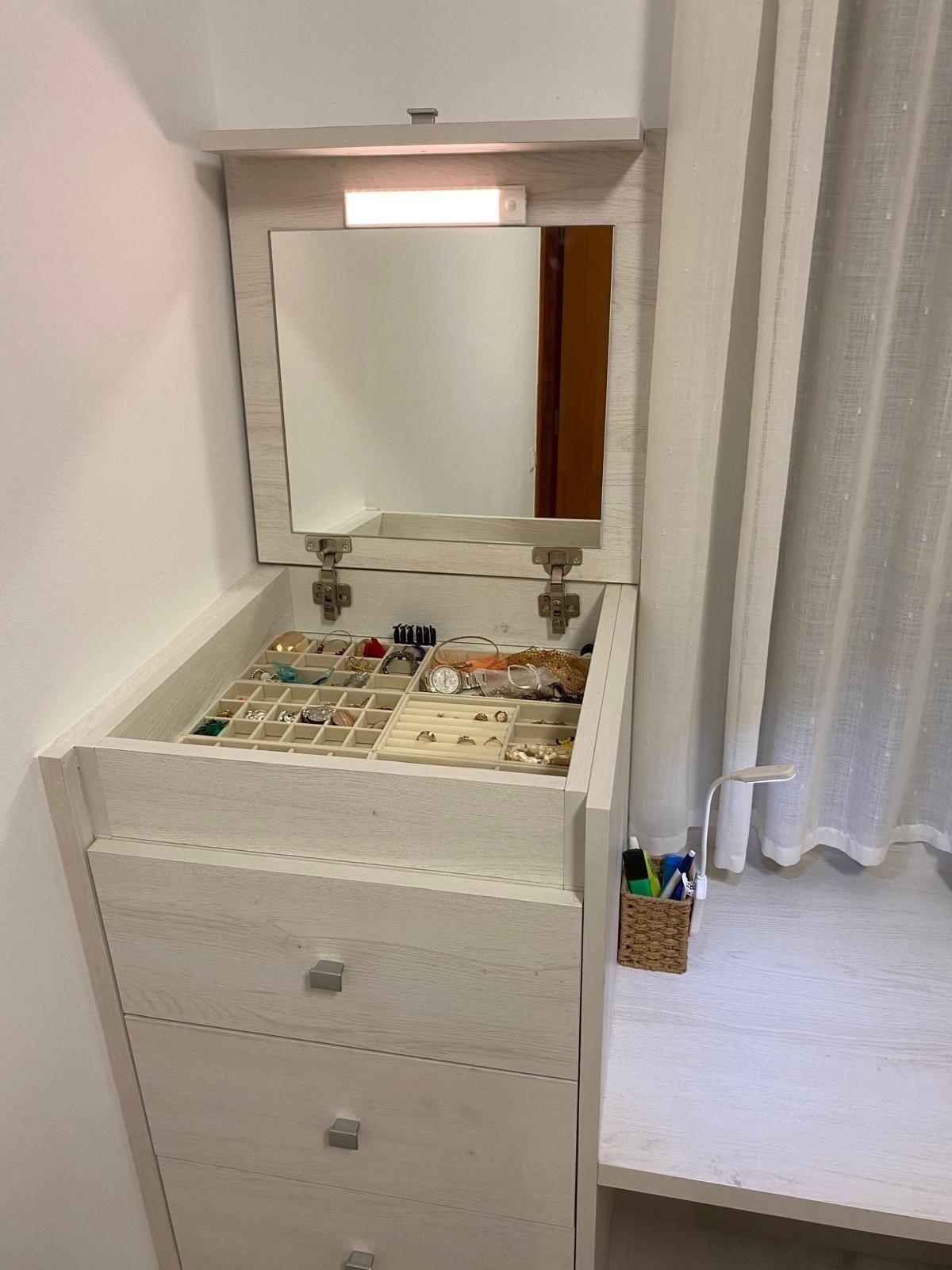 Tocador blanco con espejo y maquillaje organizado en una habitación luminosa junto a una cortina transparente.